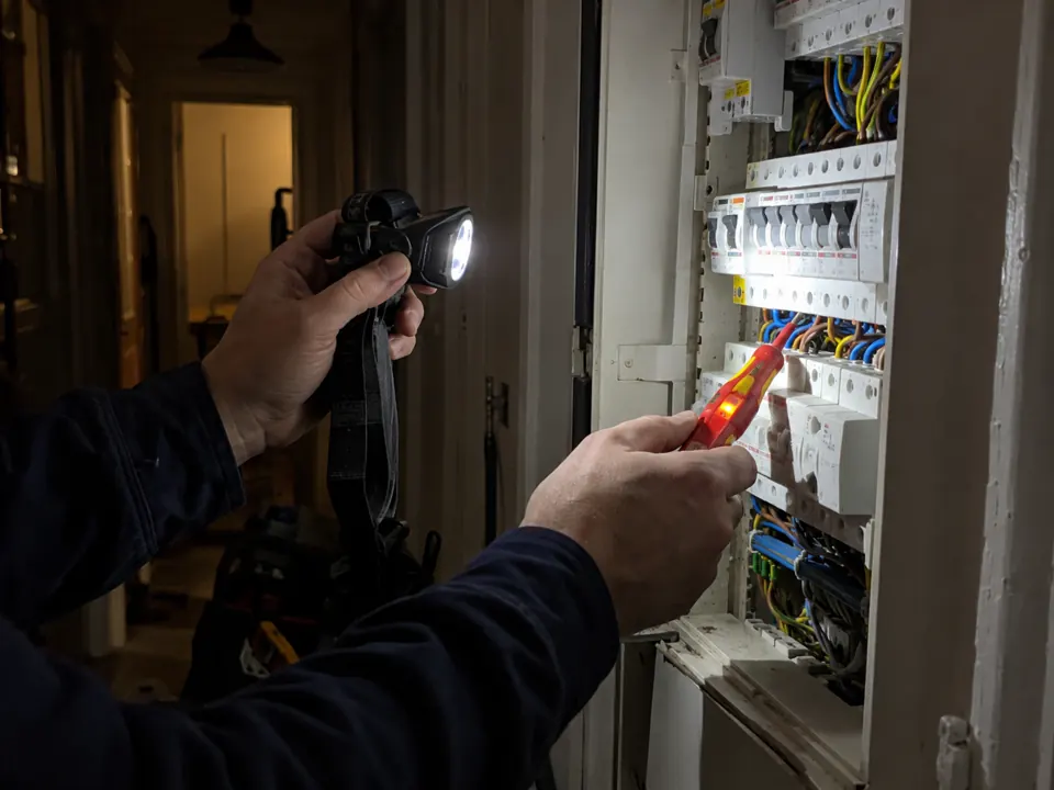 Électricien de Franck 24 vérifiant un tableau électrique avec une lampe frontale et un détecteur de tension